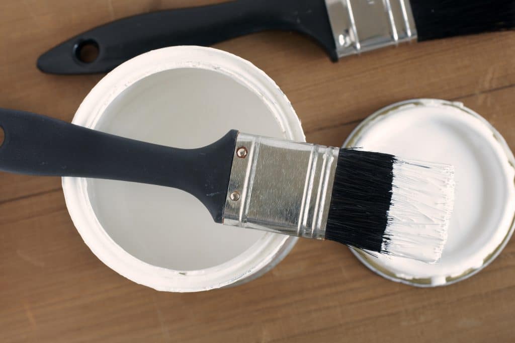 Paintbrush laying atop small can of white paint or primer